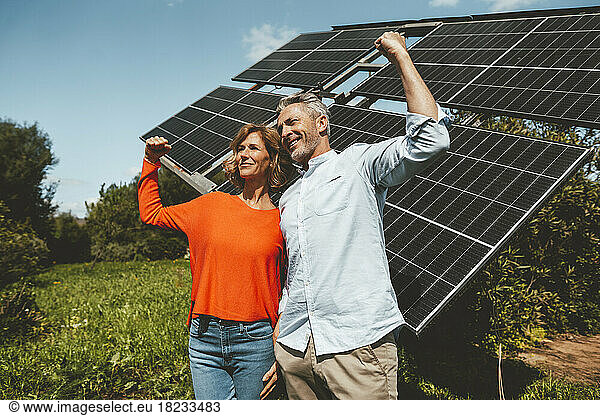 Happy mature couple flexing muscles standing in front of solar panels