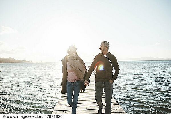 Happy mature couple holding hands walking on jetty