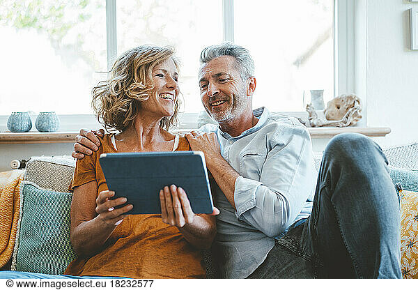 Happy mature couple sitting with tablet computer on sofa at home