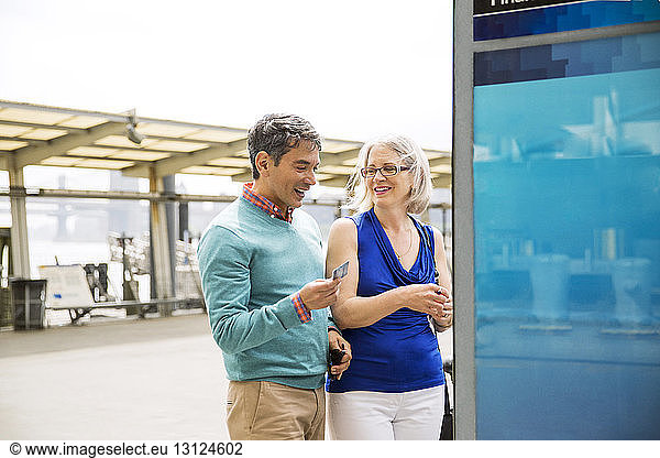 Happy mature couple standing by cash machine in city