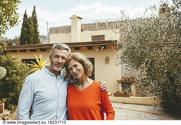 Happy mature couple standing in front of house