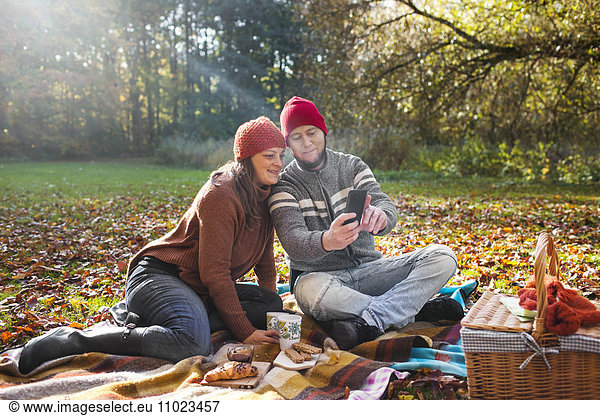 Happy mature couple taking selfie through mobile phone in forest during picnic