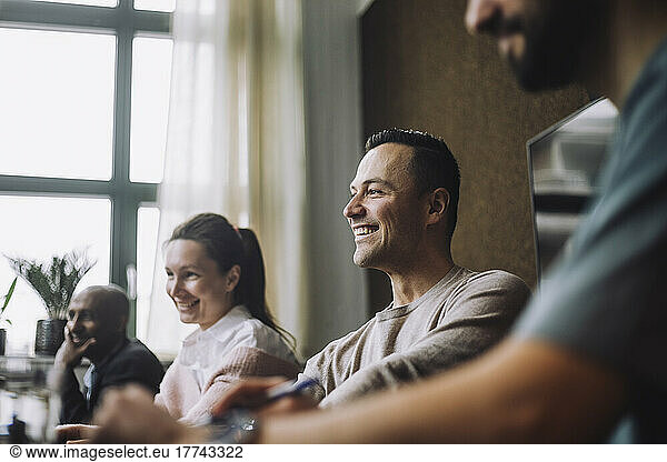Happy mature male entrepreneur sitting by colleagues during meeting in creative focus