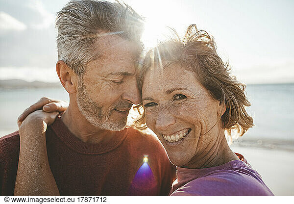 Happy mature man embracing woman at beach on sunny day