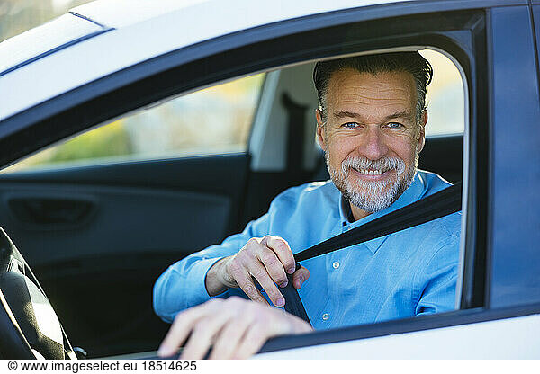 Happy mature man fastening seat belt in car