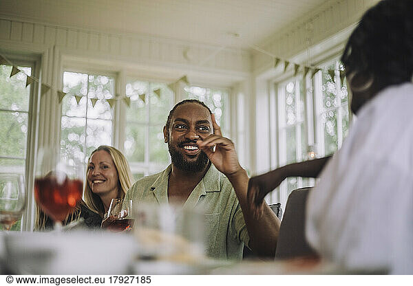 Happy mature man gesturing while talking to female friend during party at home