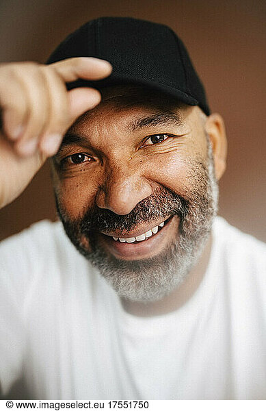 Happy mature man holding cap against brown background