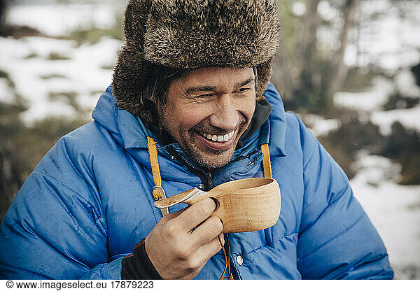 Happy mature man in warm clothing drinking tea in wooden cup