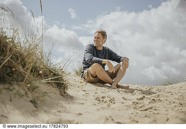 Happy mature man sitting on sand at beach