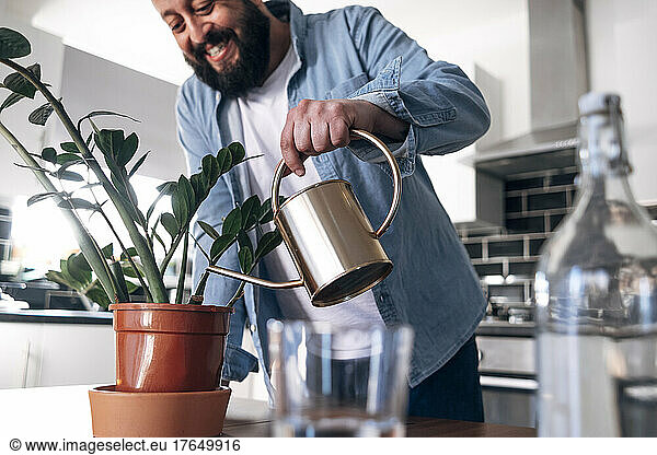 Happy mature man watering plant at home