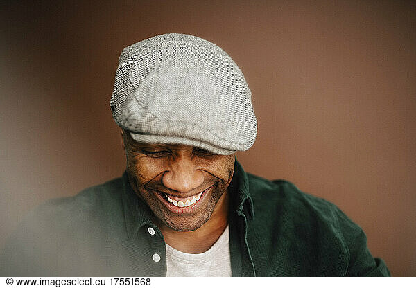 Happy mature man wearing beret looking down over brown background
