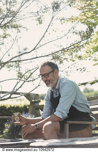 Happy mature man with coffee cup sitting in garden