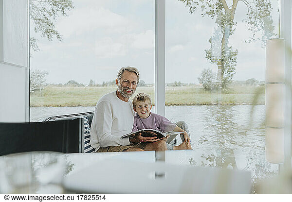 Happy mature man with son sitting on sofa at home