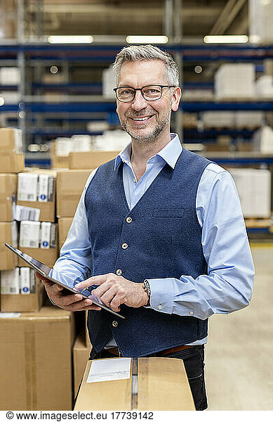 Happy mature manager with tablet PC standing in warehouse