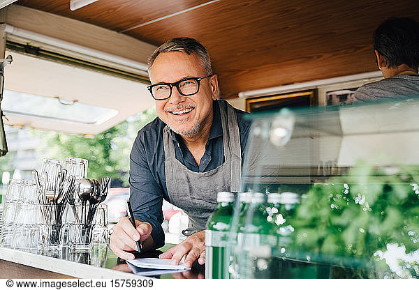 Happy mature owner standing with pen standing in food truck