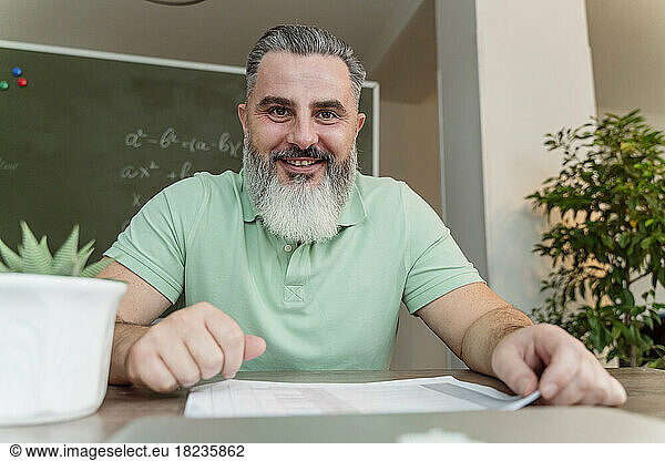 Happy mature teacher with beard at desk