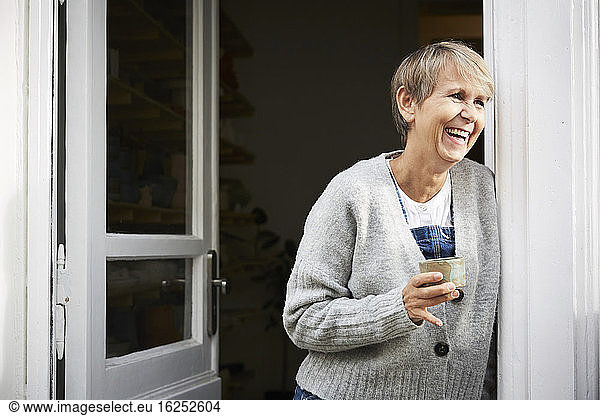 Happy mature woman having coffee at entrance of art studio