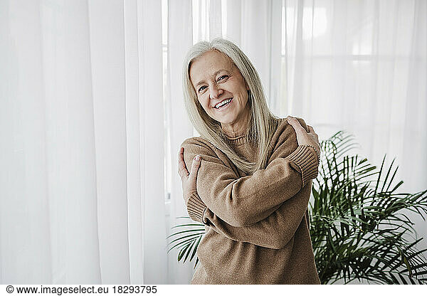 Happy mature woman hugging self at home