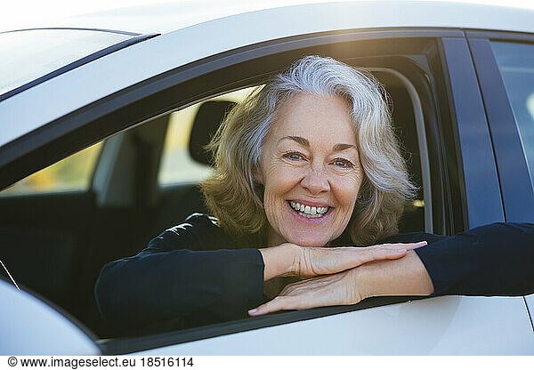 Happy mature woman leaning on car window
