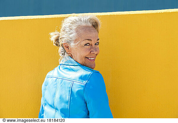 Happy mature woman looking over shoulder in front of wall