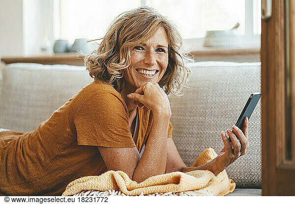 Happy mature woman lying on sofa with smart phone at home