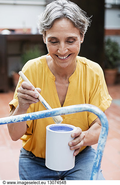Happy mature woman painting chair at yard