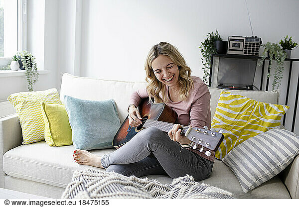 Happy mature woman playing guitar on sofa at home