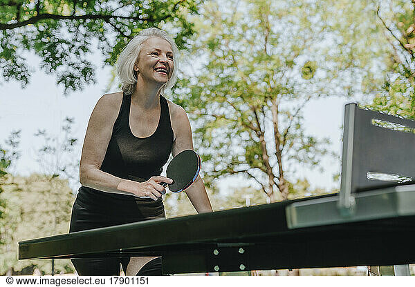 Happy mature woman playing table tennis in park