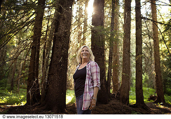 Happy mature woman standing against trees at forest