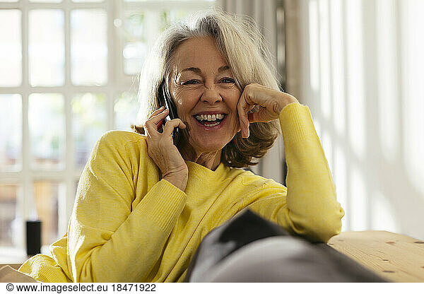 Happy mature woman talking on smart phone at home