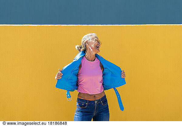 Happy mature woman wearing blue leather jacket in front of colored wall