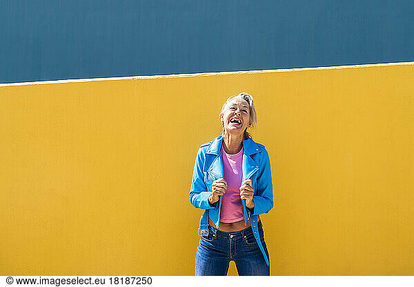 Happy mature woman wearing blue leather jacket in front of colored wall