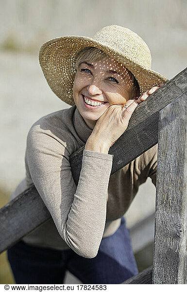 Happy mature woman wearing hat leaning on railing