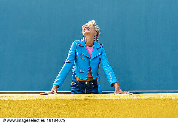 Happy mature woman wearing leather jacket in front of blue wall