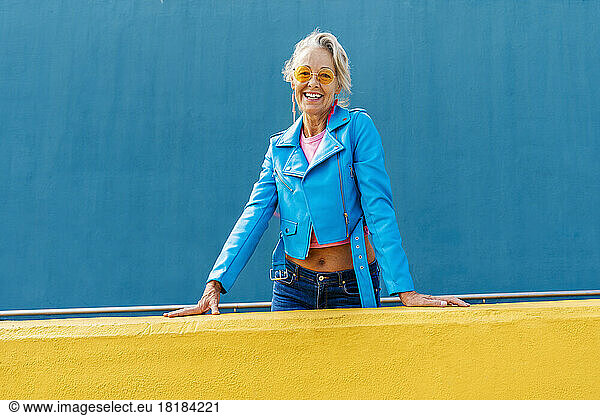Happy mature woman wearing sunglasses in front of blue wall