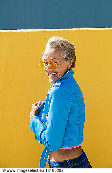 Happy mature woman wearing sunglasses in front of colored wall