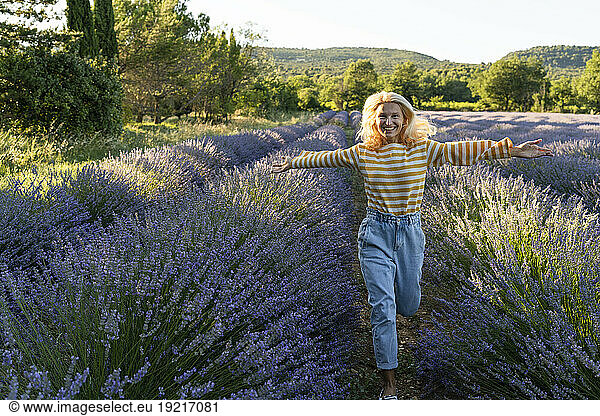 Happy mature woman with arms outstretched running in lavender field