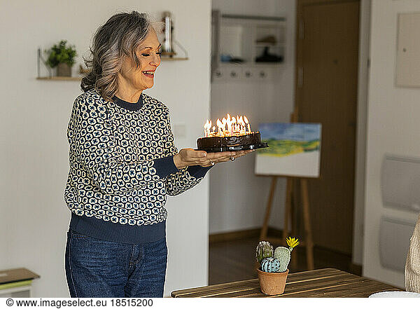 Happy mature woman with birthday cake standing at home
