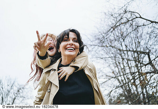 Happy mature woman with daughter showing peace sign gesture under sky