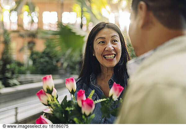 Happy mature woman with flowers looking at boyfriend on Valentine's Day