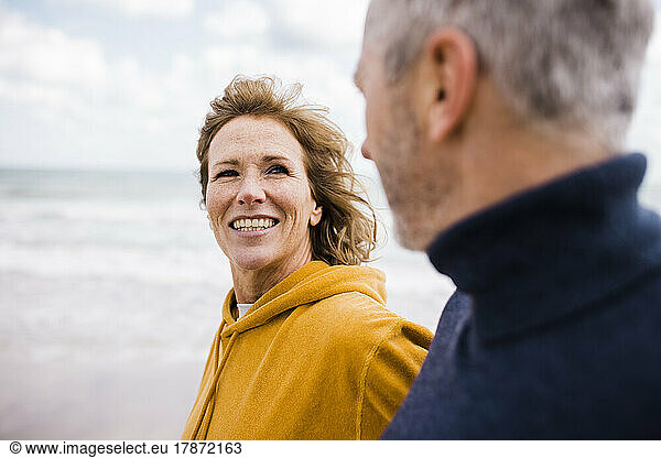 Happy mature woman with man walking at beach