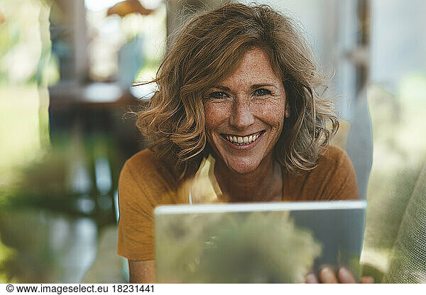 Happy mature woman with tablet PC seen through glass window