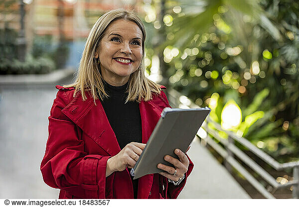 Happy mature woman with tablet PC standing on footpath