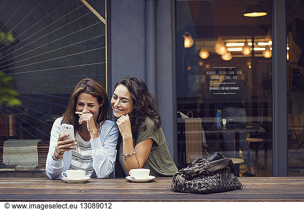 Happy mature women using smart phone at sidewalk cafe