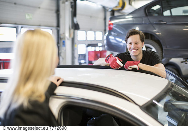 Happy mechanic looking at female customer over car at workshop