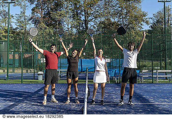 Happy men and women with arms raised standing at sports court