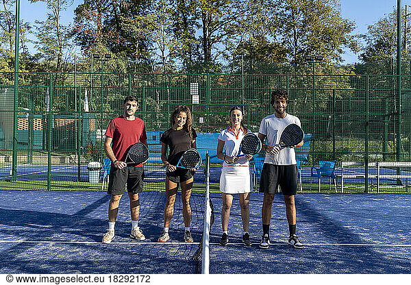 Happy men and women with paddle tennis rackets standing at sports court