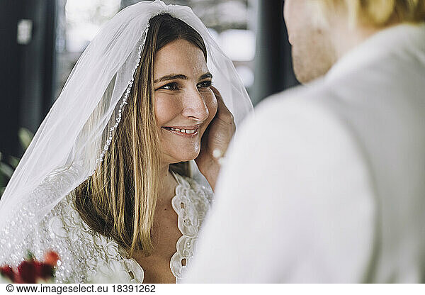 Happy mid adult bride in wedding dress looking at groom