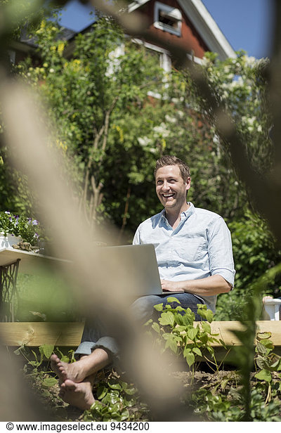 Happy mid adult man with laptop relaxing on terrace