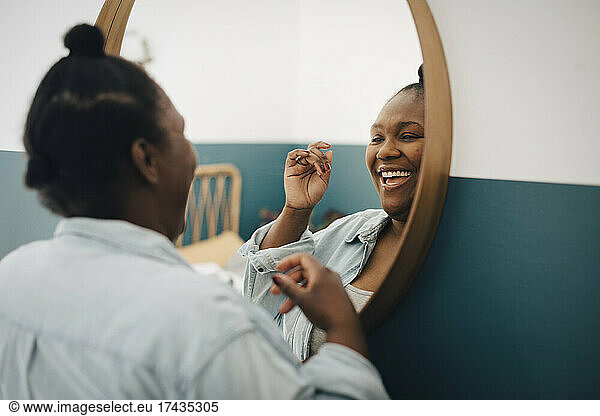 Happy mid adult woman looking in mirror at home